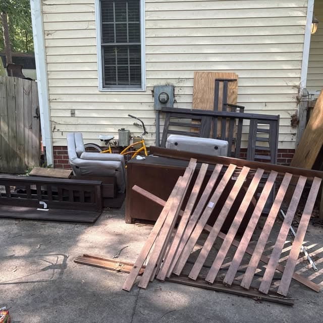 Furniture, bed rails, and scrap wood piled in a backyard before removal