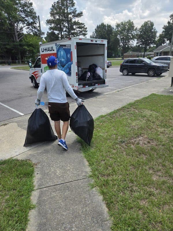 Got Junk NC crew member carrying two bags of household junk to a box truck on a residential street