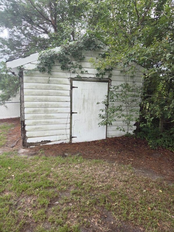 Overgrown backyard storage shed with mouldy white siding and vines, before Got Junk NC tore it down