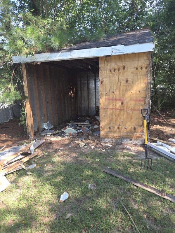 Backyard shed part-way through teardown with the siding stripped off and the frame exposed
